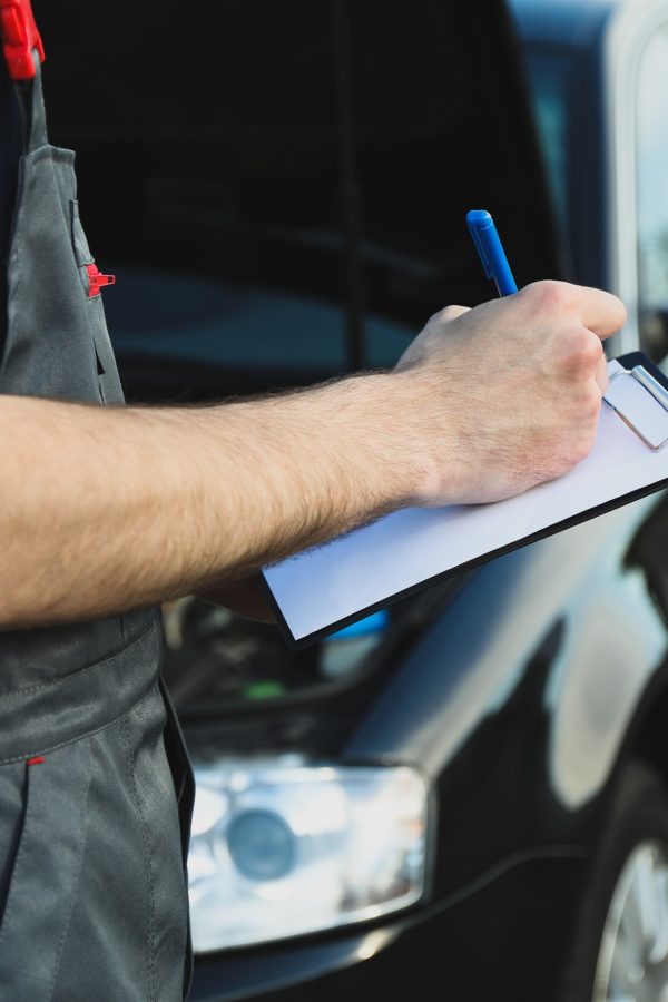 a-man-in-overalls-writes-to-a-clipboard-mechanic-car-inspection.jpg